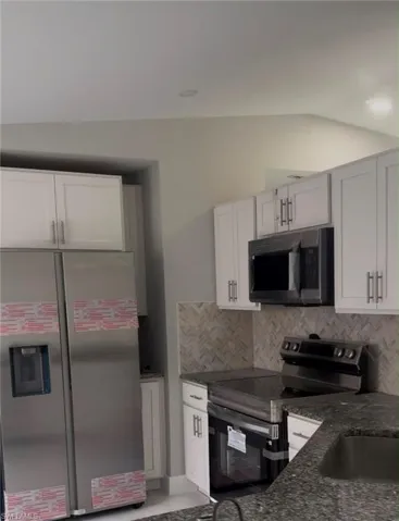 Kitchen featuring white shaker cabinetry, stainless steel appliances, dark granite countertops, and a herringbone-patterned tile backsplash