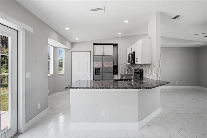 Kitchen featuring a granite countertop island with integrated sink, white cabinetry, and stainless steel appliances