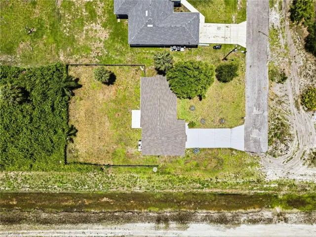 Aerial perspective showcasing a property with a gray shingle roof, concrete driveway, and surrounding green space