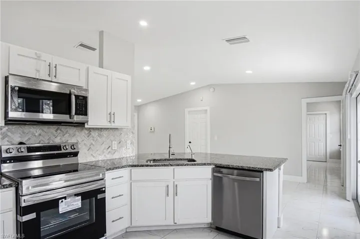 Modern kitchen featuring white cabinetry, stainless steel appliances, a herringbone tile backsplash, and speckled countertops