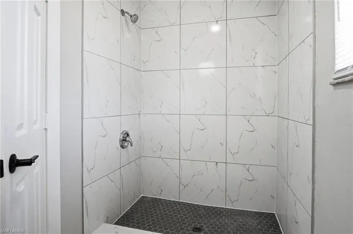 Walk-in shower featuring large format white tile walls with grey veining, a dark hexagonal tile floor, and chrome fixtures