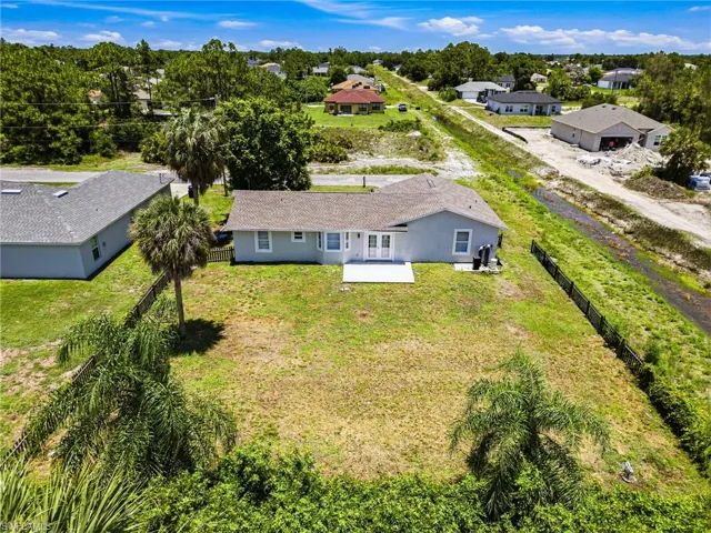 Expansive rear yard featuring a light gray exterior, two mature palm trees, a dark perimeter fence, and a concrete patio