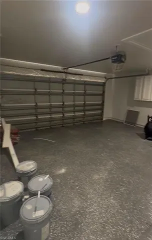 Spacious garage featuring a durable speckled epoxy floor, overhead lighting, an automatic garage door opener, and built-in white cabinetry