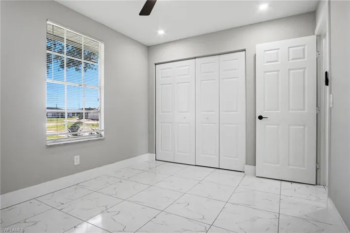 Bedroom featuring a window with horizontal blinds, white bi-fold closet doors, a six-panel interior door with black hardware, recessed ceiling lighting, and a ceiling fan