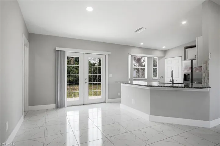 Spacious interior featuring marble-look tile flooring, recessed lighting, double French doors, a kitchen island with granite-look countertop, and a bay window