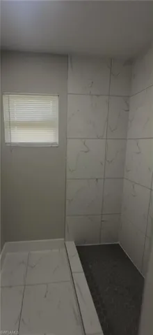 Walk-in shower with white veined wall tiles and dark hexagonal floor tiles