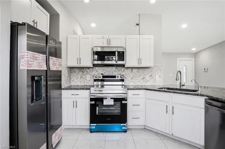 Contemporary kitchen featuring white cabinetry, stainless steel appliances, speckled countertops, a herringbone tile backsplash, and recessed lighting