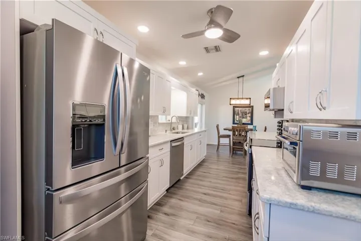 Kitchen with appliances with stainless steel finishes, decorative light fixtures, light hardwood / wood-style floors, white cabinetry, and lofted ceiling