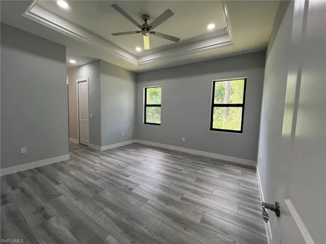 Empty room featuring a raised ceiling, recessed lighting, wood finished floors, a ceiling fan, and crown molding