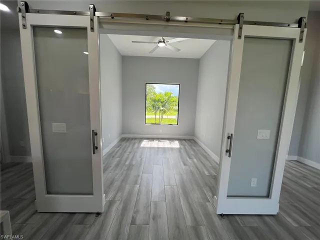 Empty room with a barn door, wood finished floors, and a ceiling fan