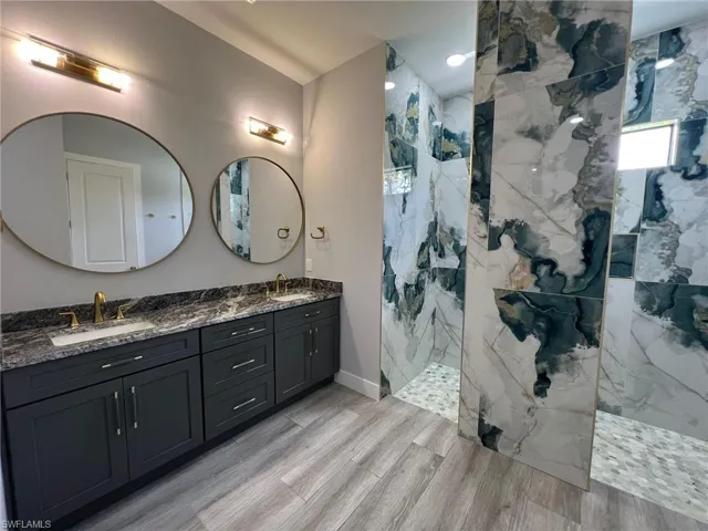 Bathroom featuring double vanity, a marble finish shower, and wood finished floors