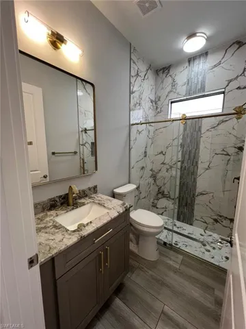 Full bath with a marble finish shower, vanity, and wood finished floors