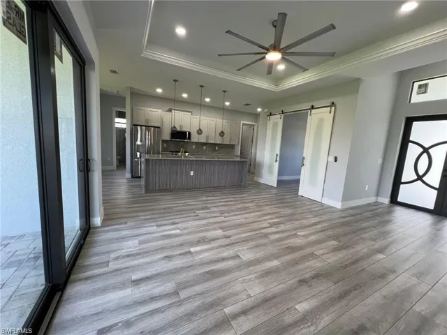 Kitchen with a barn door, a center island with sink, a raised ceiling, appliances with stainless steel finishes, and open floor plan
