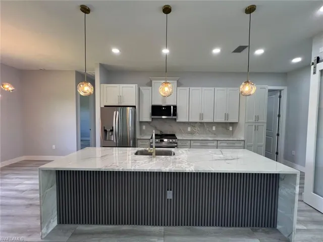 Kitchen featuring stainless steel appliances, backsplash, a large island with sink, white cabinetry, and light stone counters