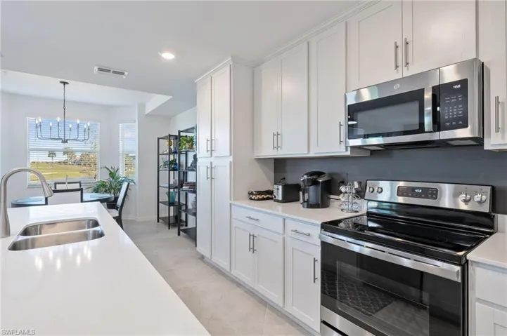 Kitchen with white cabinets, pendant lighting, stainless steel appliances, sink, and a notable chandelier