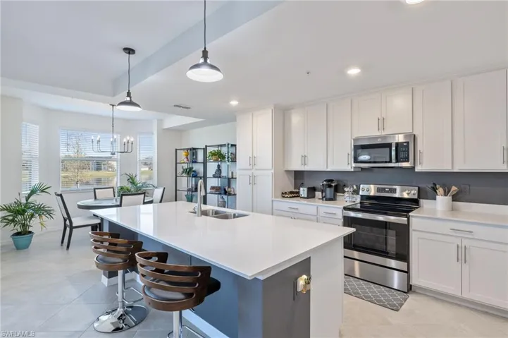 Kitchen featuring hanging light fixtures, sink, a kitchen island with sink, white cabinetry, and appliances with stainless steel finishes