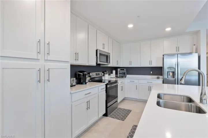 Kitchen with appliances with stainless steel finishes, sink, light tile patterned floors, and white cabinets