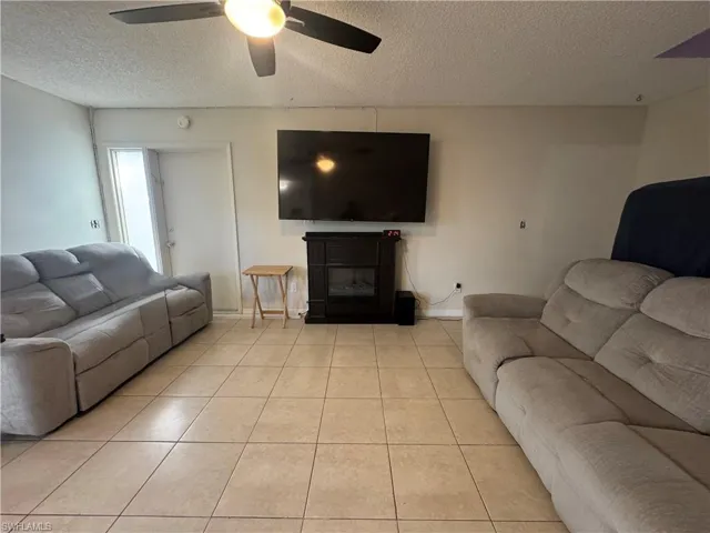 Living area with a textured ceiling, a glass covered fireplace, tile patterned floors, and ceiling fan
