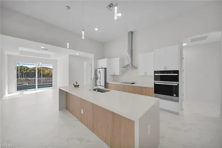 Two tone kitchen featuring dual tone cabinets, light marble finish flooring, stainless steel appliances, hanging light fixtures, and light stone countertops