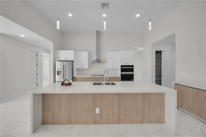 Dual tone kitchen featuring a large island with sink, light stone countertops, light marble finish flooring, black appliances, and two tone cabinets