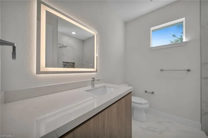Bathroom with a marble finish shower, light marble finish floors, and vanity