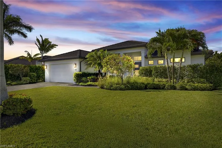View of the front of the home with stucco siding, brick paved driveway, landscaped lawn, two car garage, and concrete tile roof
