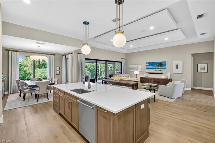 Kitchen with dishwasher, light engineered wood floors, healthy amount of natural light from southern exposure, expanded center island with sink, and designer pendant lighting