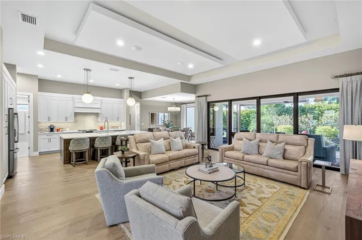 Living room with light wood finished floors, recessed lighting, designer chandelier, and custom tray/drop ceiling open to the chef's kitchen