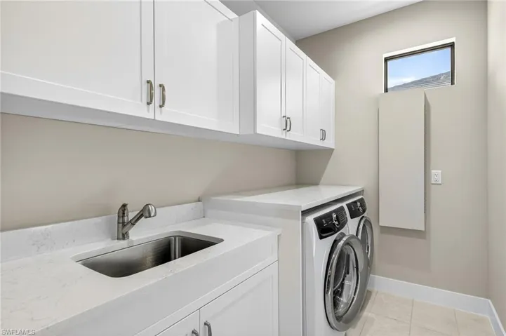 Laundry room with Electrolux washer and dryer, additional cabinet space, laundry sink, and built in ironing table and hiddent hanging laundry extenders and closet