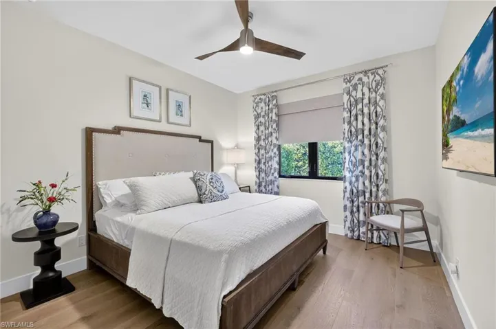 Guest bedroom with engineered wood floors, ceiling fan, and custom window treatments with blackout shade