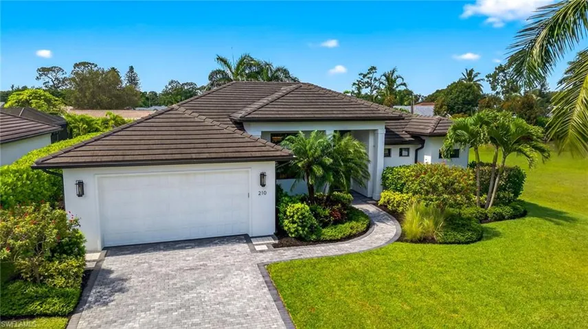 Single story home featuring a tiled roof, brick paved driveway, stucco siding, professionally landscaped lawn, and a two car extended garage