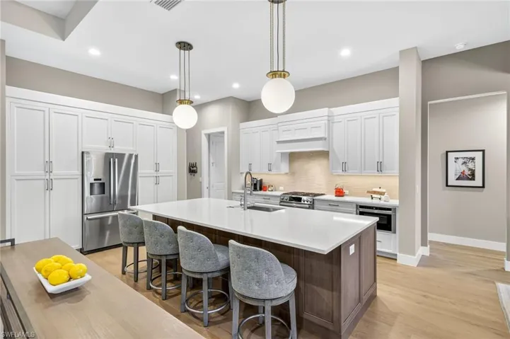 Kitchen featuring Bosch appliances with stainless steel finishes, gas cooktop, decorative backsplash, a kitchen breakfast bar, center island with sink, and custom cabinets with built-ins
