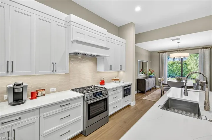Kitchen featuring gas cooktop range, backsplash, white cabinetry with pull out pots and pans drawers, under cabinet lighting, and light engineered wood flooring