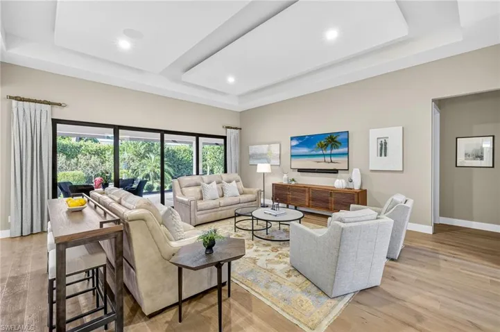 Living area great room with a custom tray/drop ceiling, light engineered wood flooring, and recessed lighting and 16' sliding glass entry onto the screened lanai