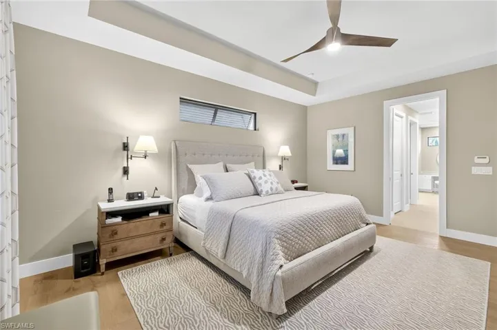 Owners suite with light engineered wood flooring, tray ceiling, and ceiling fan