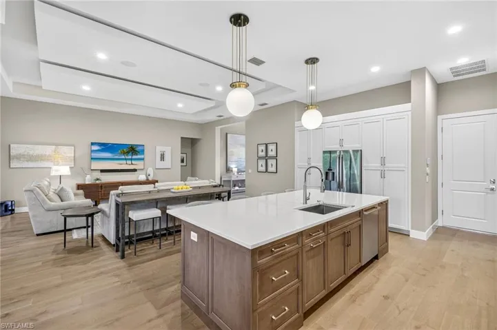 Kitchen featuring refrigerator with french doors, ice maker/dispenser, dishwasher, custom cabinetry with built-ins, kitchen island with sink, and open floor plan