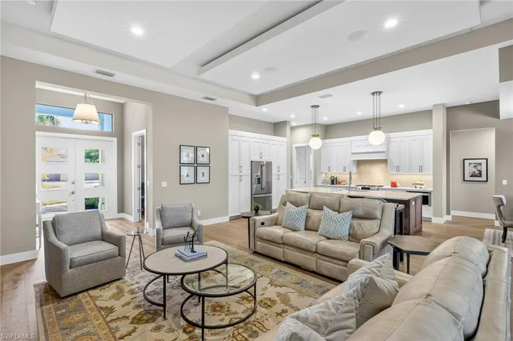 Living room with light wood finished floors, recessed lighting, designer chandelier, and custom tray/drop ceiling open to the chef's kitchen
