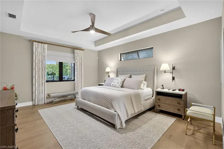 Bedroom featuring a tray ceiling, light wood-style flooring, and ceiling fan