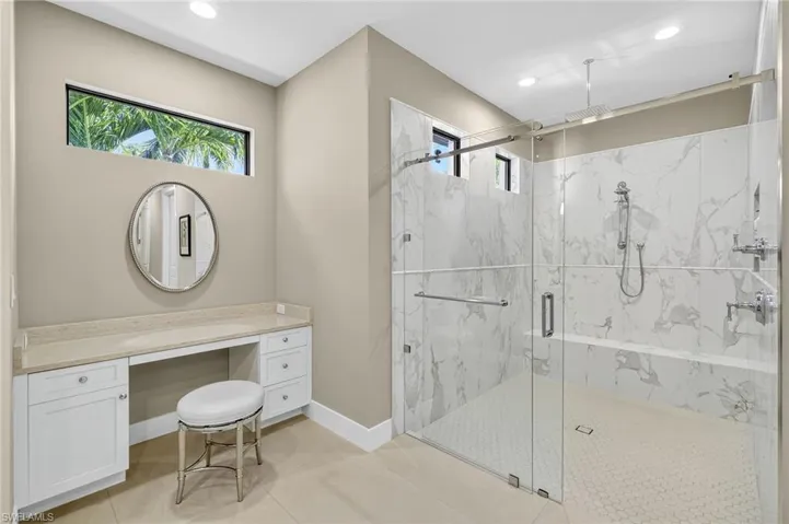 Marble look tile finish shower with two shower heads, glass door entry, make-up vanity, and recessed lighting