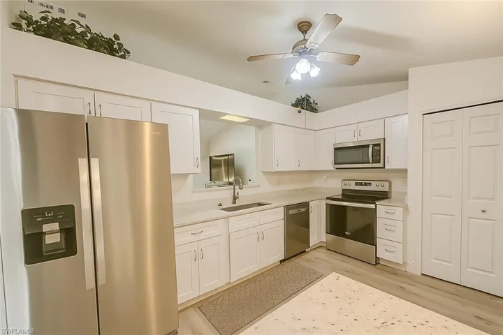 Kitchen featuring appliances with stainless steel finishes, light wood-type flooring, white cabinetry, lofted ceiling, and a ceiling fan