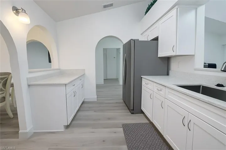 Kitchen featuring white cabinetry, light stone counters, light wood finished floors, arched walkways, and freestanding refrigerator