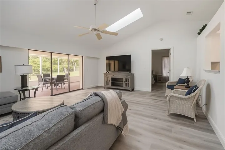 Living room with a skylight, light wood finished floors, high vaulted ceiling, and ceiling fan