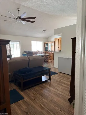 Living area featuring wood finished floors, a textured ceiling, a ceiling fan, and vaulted ceiling