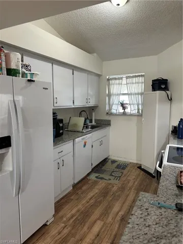 Kitchen with white cabinets, white stove, a textured ceiling, fridge, and dark wood-type flooring