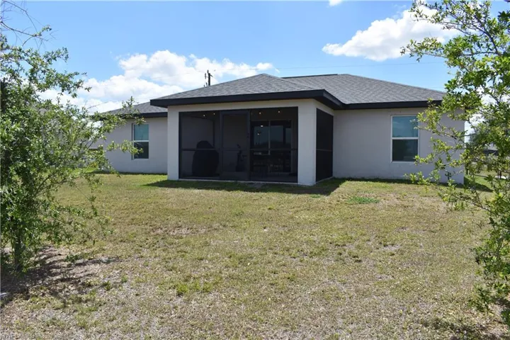 Back of property with a shingled roof, a lawn, stucco siding, and a sunroom