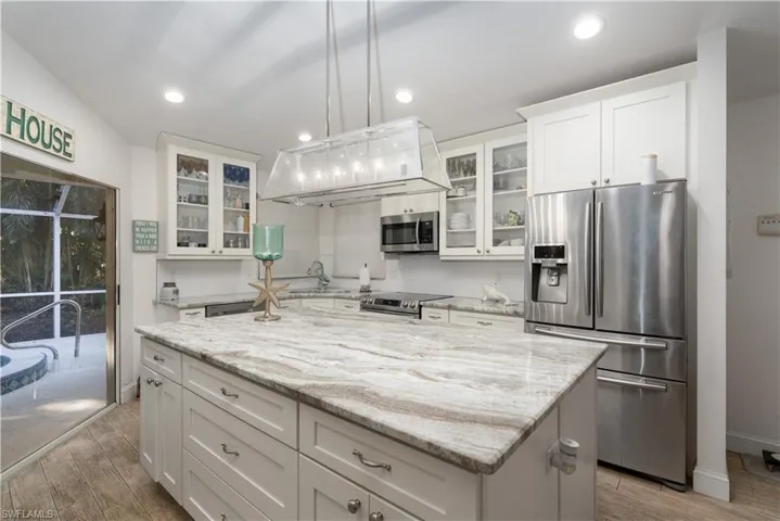 Kitchen featuring stainless steel appliances, a center island, light stone counters, white cabinets, and recessed lighting