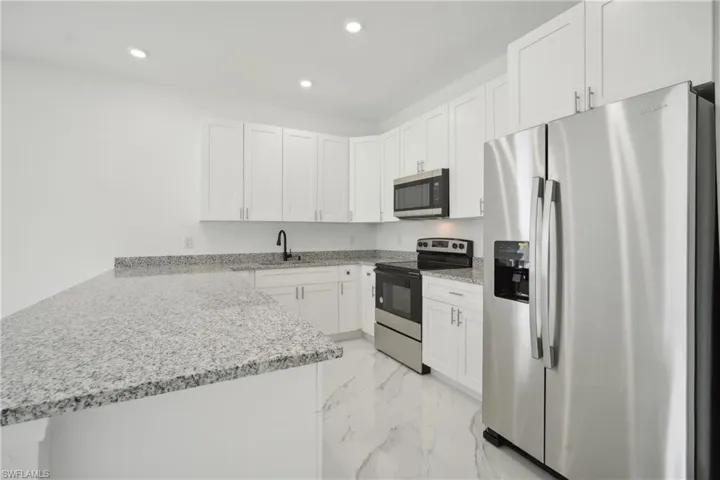 Kitchen with white cabinetry, light stone counters, kitchen peninsula, stainless steel appliances, and sink
