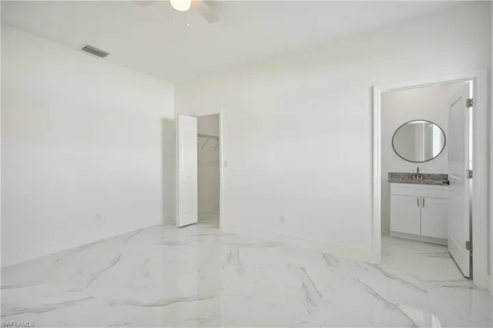 Unfurnished bedroom with ceiling fan, connected bathroom, sink, a walk in closet, and a closet