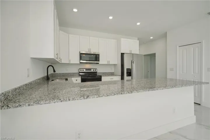 Kitchen featuring white cabinets, light stone counters, kitchen peninsula, and appliances with stainless steel finishes