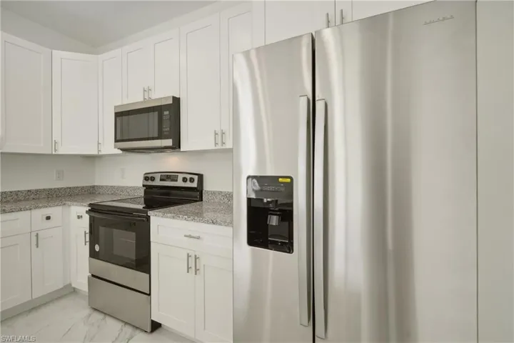 Kitchen with light stone countertops, stainless steel appliances, and white cabinets